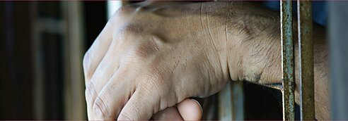 A prisoner holds their hands between the bars